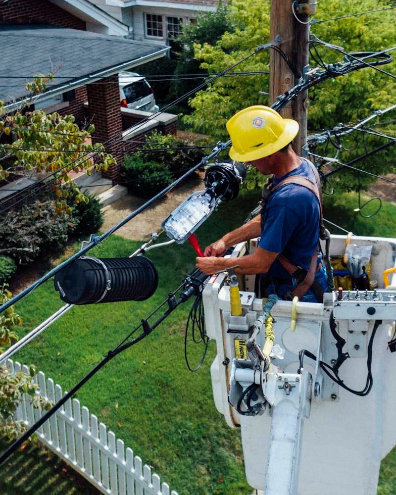 Electrician in a bucket lift repairing power lines from a utility pole in a suburban neighborhood.